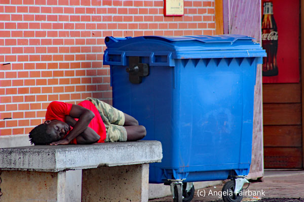boy sleeping near garbage bin